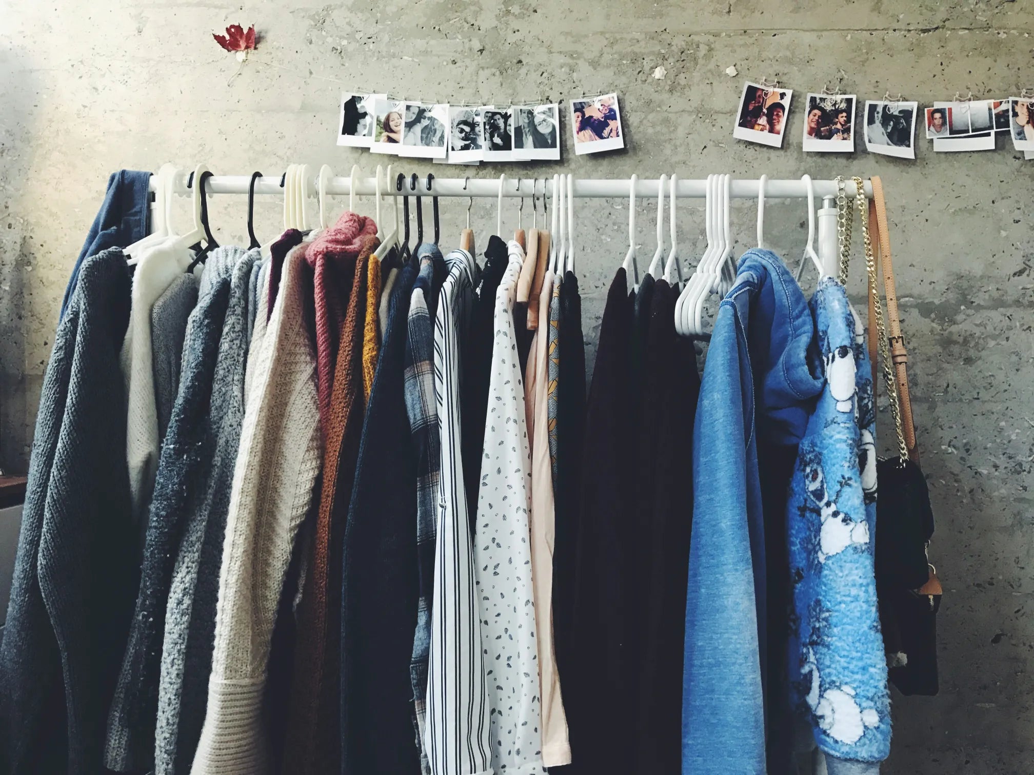 Clothing rack with various garments against a concrete wall with hanging photos.